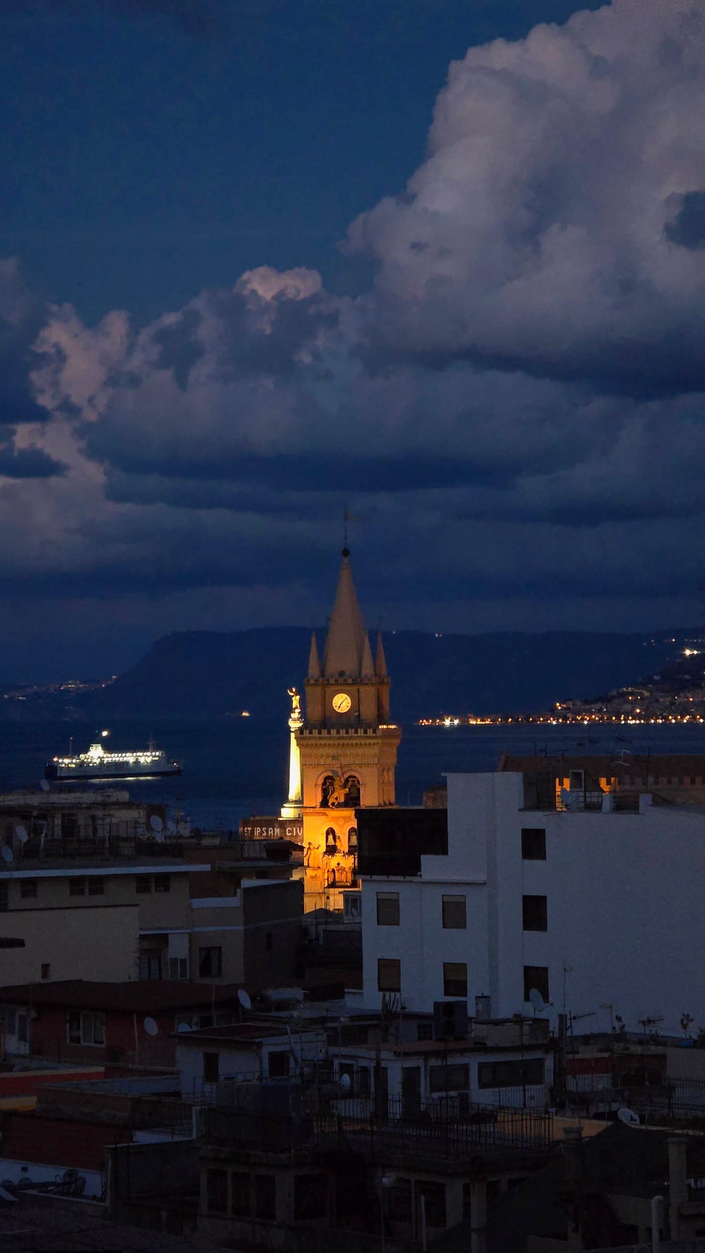 The cathedral's bell tower in Messina at dusk, with a ferry crossing the Strait